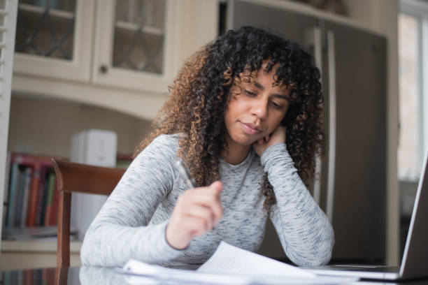 A young and attractive woman of African descent sits at her kitchen table one day. She is filling out her tax forms thoughtfully. She is focused and attentive to what has to be done. She looks relaxed and calm