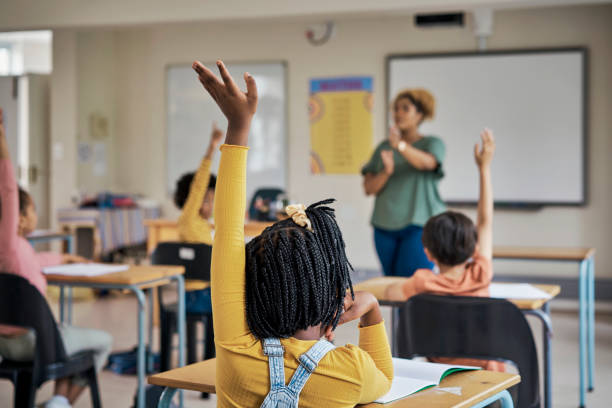 Questions, teacher or education at school with kids hands raised to answer English language assessment. Classroom, learning or tutor teaching summary information to smart and clever group of children