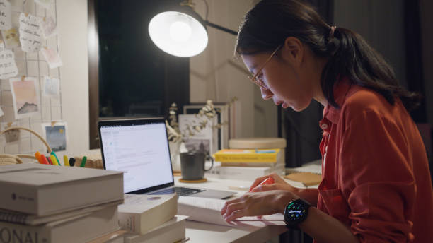 Young Asian woman wear casual sit front of desk with computer laptop and think create on work idea in living room at house at night. Work from home concept.