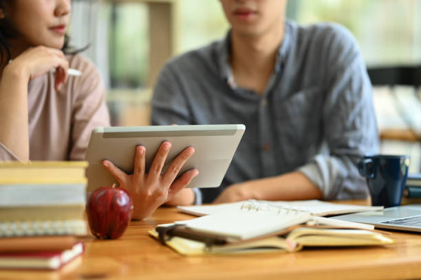 Cropped shot of college students using digital tablet, preparing for exam together in the campus.