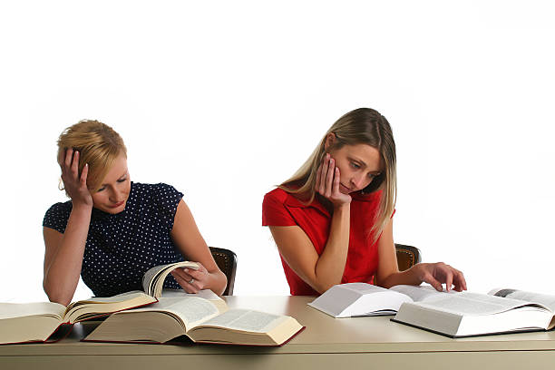 Two girls studying from big books in library