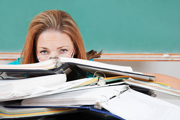 Woman hiding behind school binders in classroom.