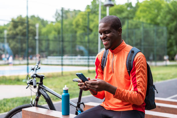 Man in athletic gear checking his phone while resting in a park. Bicycle and water bottle visible.
