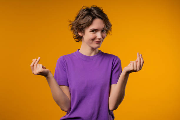 30s woman with money gesture on yellow studio background. Smart lady smiles slyly, she has idea how to earn. Profitable investments, stock market game, cryptocurrency mining