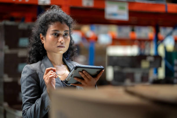 Black Warehouse worker using a digital tablet for quality control and inventory management. Wearing reflective safety clothing while inspecting cargo boxes in a distribution warehouse. Ensuring efficiency, freight transportation, and supply chain accuracy.